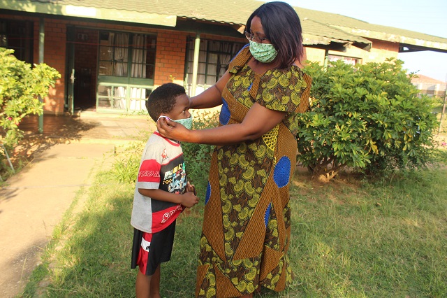 SOS mother Phoebe helps her youngest put on a protective mask