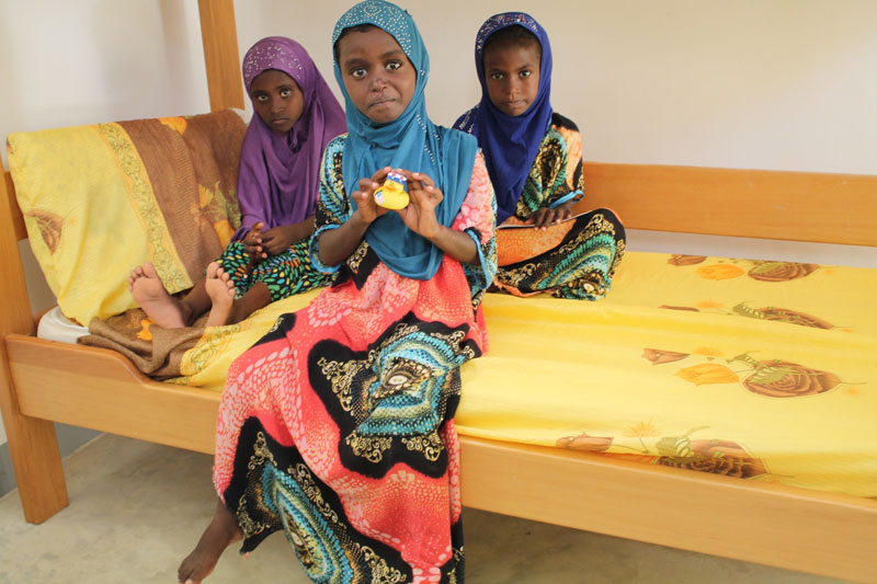 Rara sitting on a bed with her SOS siters in Tadjourah, Djibouti