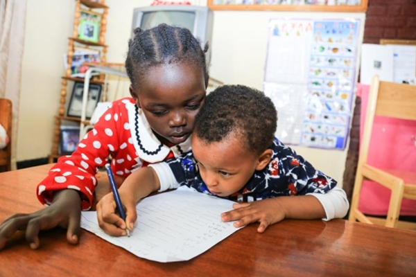 Young girl in Ethiopia helps her younger brother with his school work.
