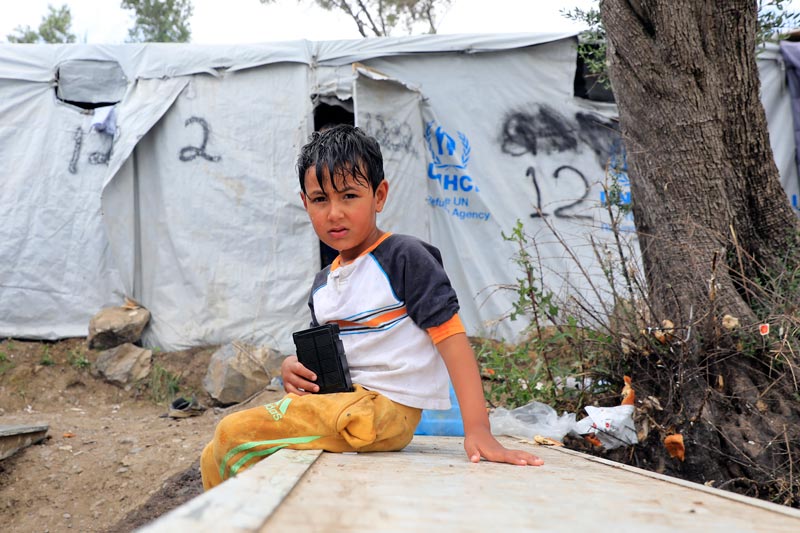 Boy sitting outside in a refugee camp in Moria, Greece