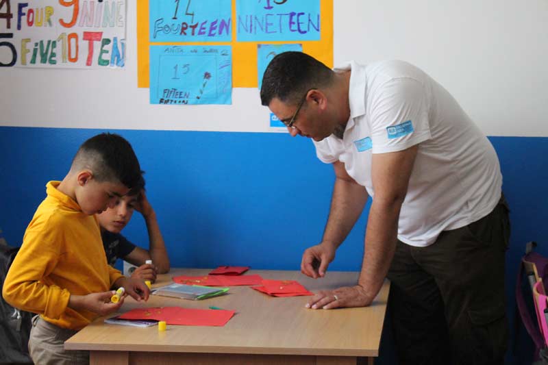 Cultural mediator Mahmoud ElShair helps children in school to accomplish their task.