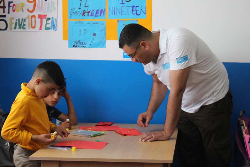 Cultural mediator Mahmoud ElShair helps children in school to accomplish their task.