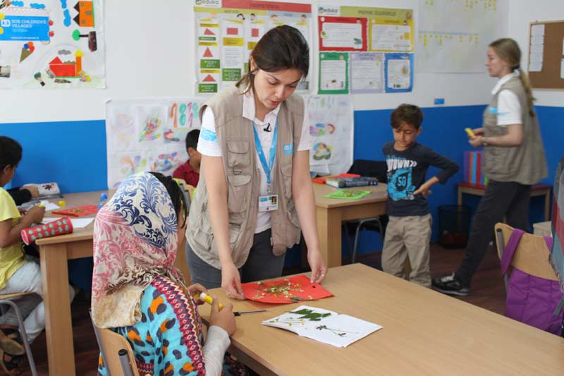 The topic of the unit today is “Herbarium”. Children are creating a page with dried flowers. Educator Jelena Zdravković talks to a girl from Afghanistan how to prepare a nice picture that she can give to her mother as a present.