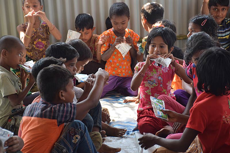 Enfants réfugiés rohingyas mangeant des paquets de nourriture dans l'espace ami des enfants SOS au Bangladesh