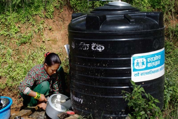 Woman getting water from water tank with SOS Nepal logo