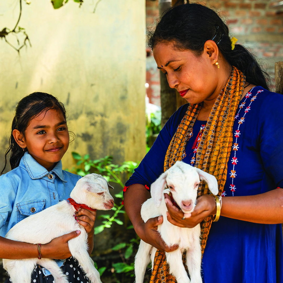 Mother and daughter holding baby goats outside their home in India