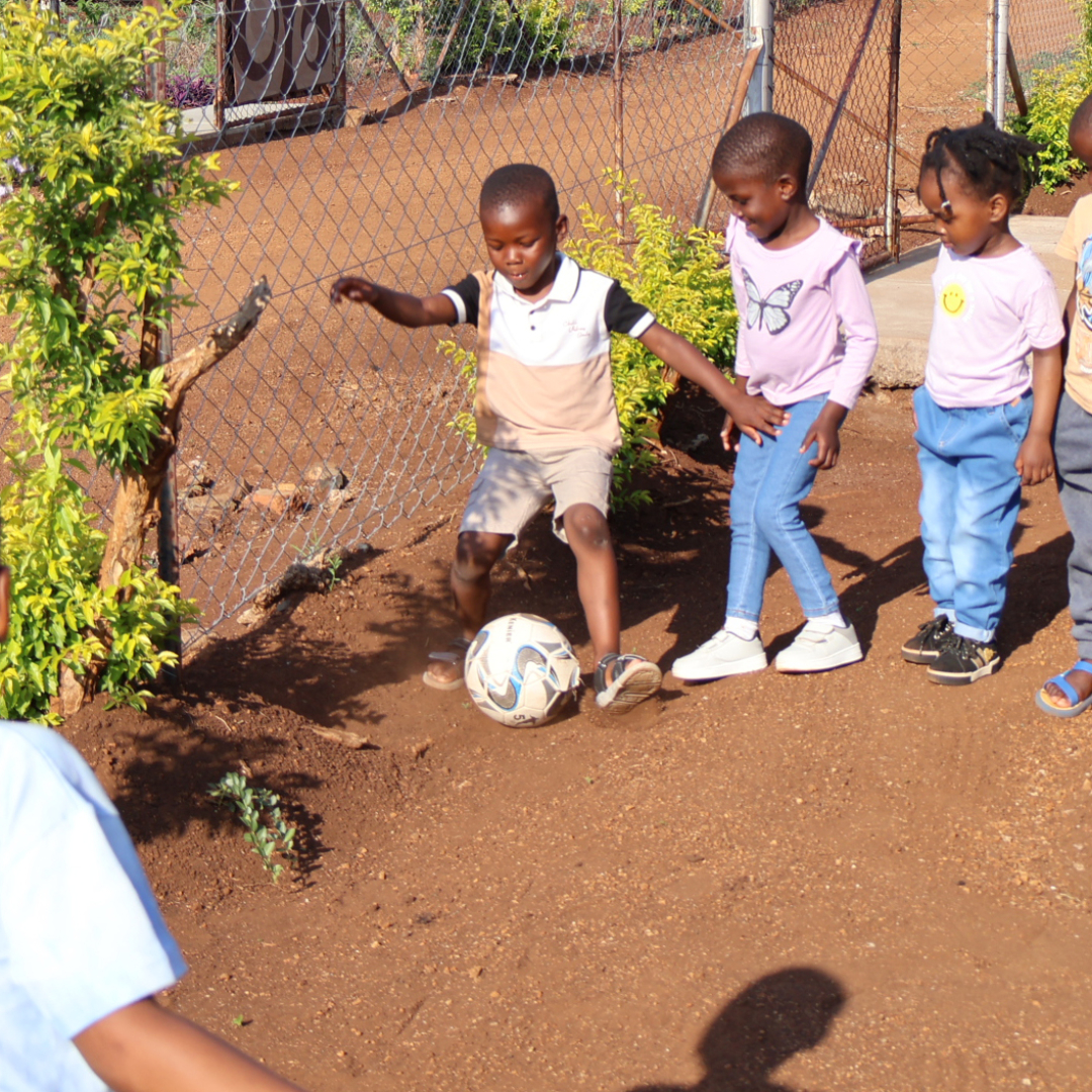 A group of young children taking turns kicking the soccer ball in Eswatini.