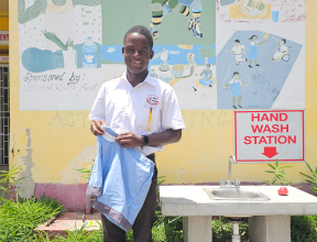 In Jamaica, Kyle stands outdoors holding a pair of blue shorts he made at school.