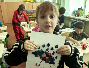 A young Ukrainian boy holding up a piece of art they have created.