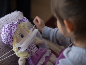 A child puts a protective mask on her toy.