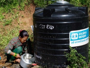 Woman getting water from water tank with SOS Nepal logo