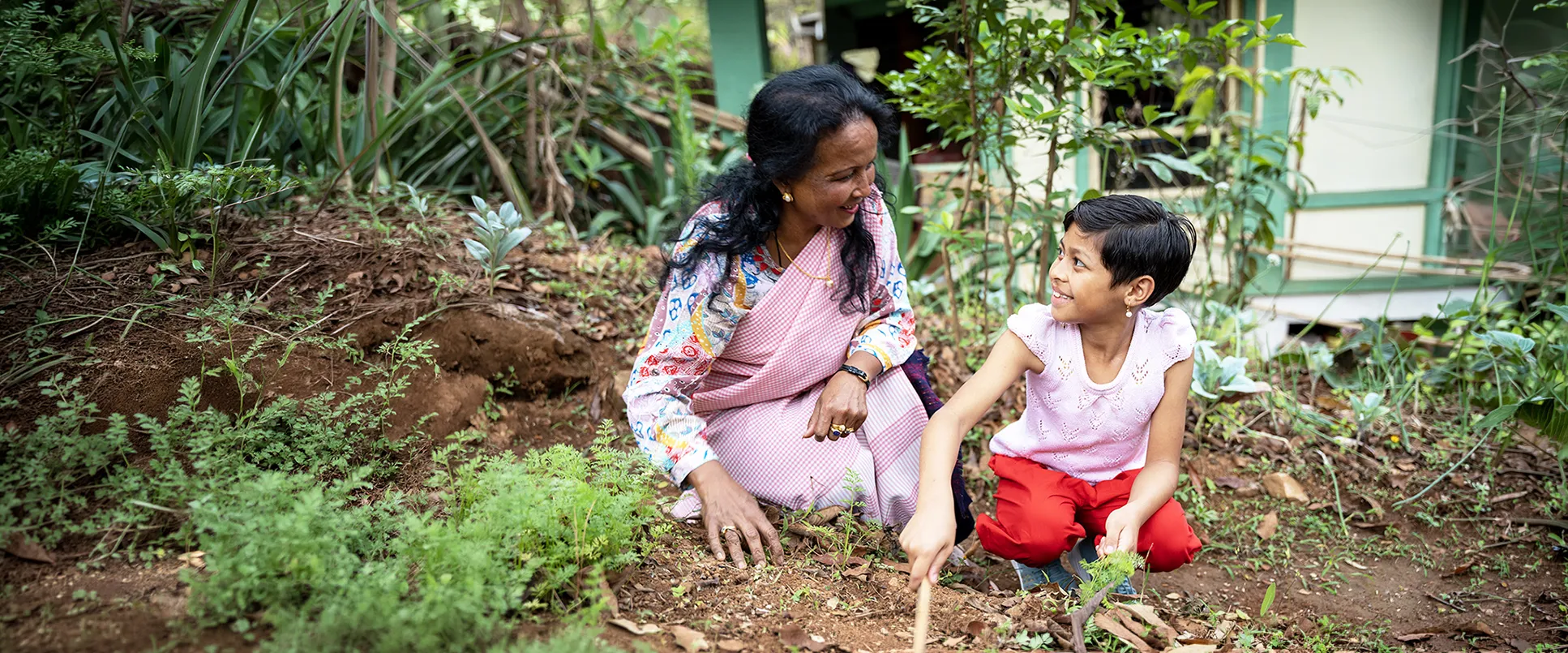 Mother and daughter in India looking at each other lovingly while working in the garden