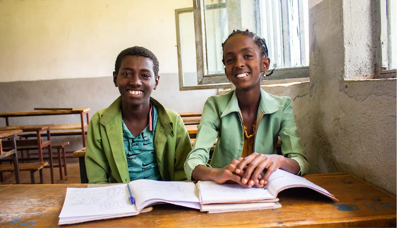 Two students with open books in a classroom