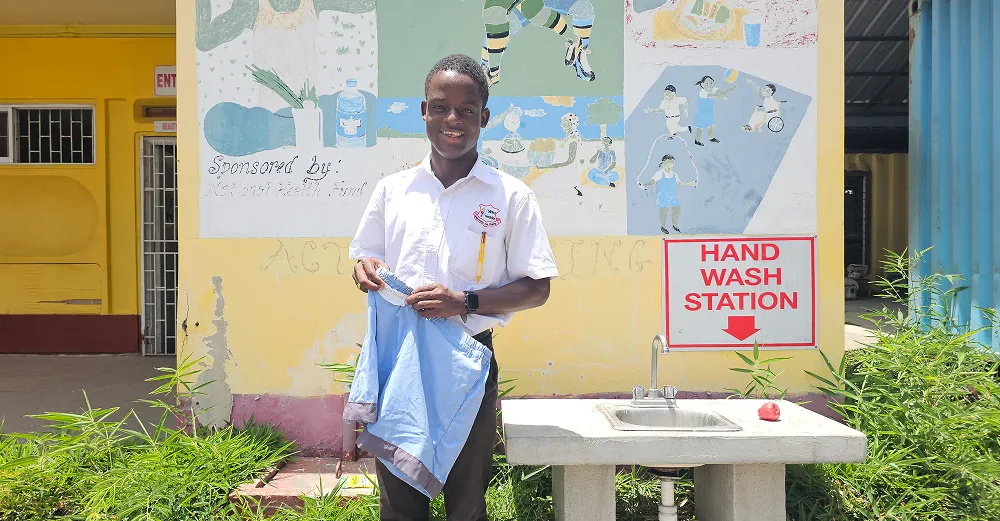 In Jamaica, Kyle stands outdoors holding a pair of blue shorts he made at school.