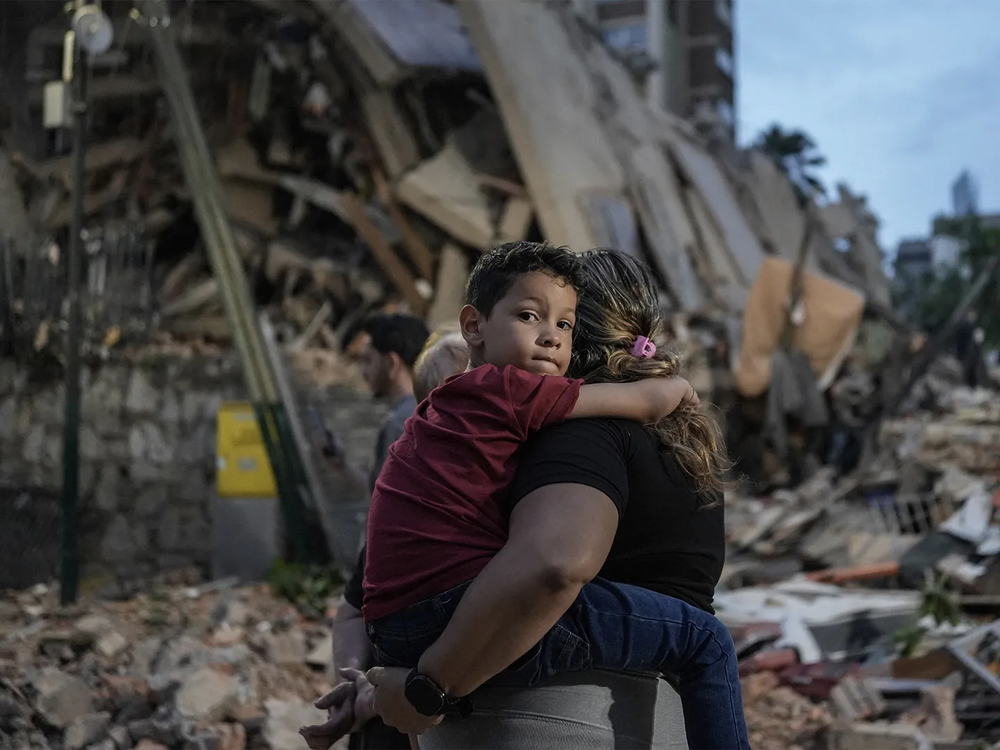 Mother holding child tightly in front of rubble caused by earthquake