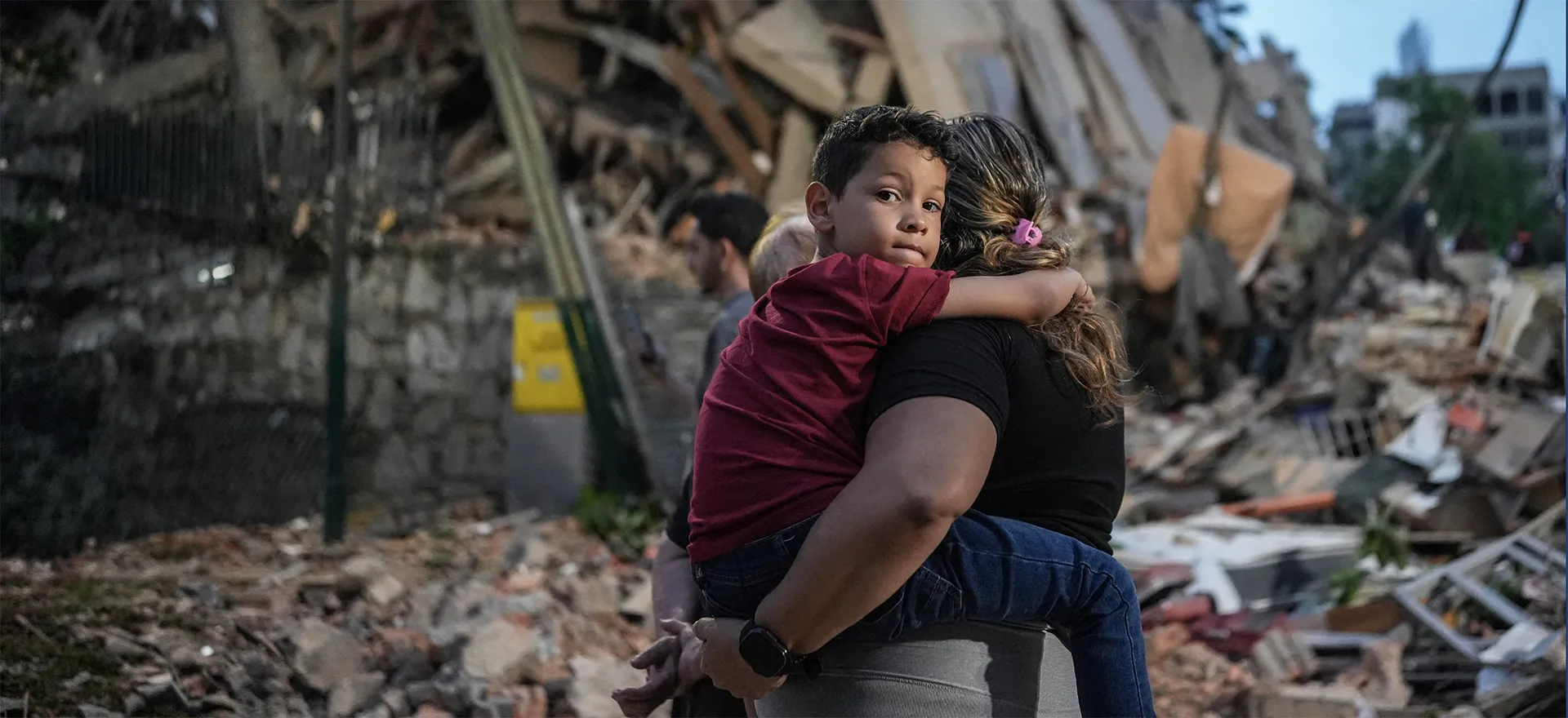Mother holding child tightly in front of rubble caused by earthquake