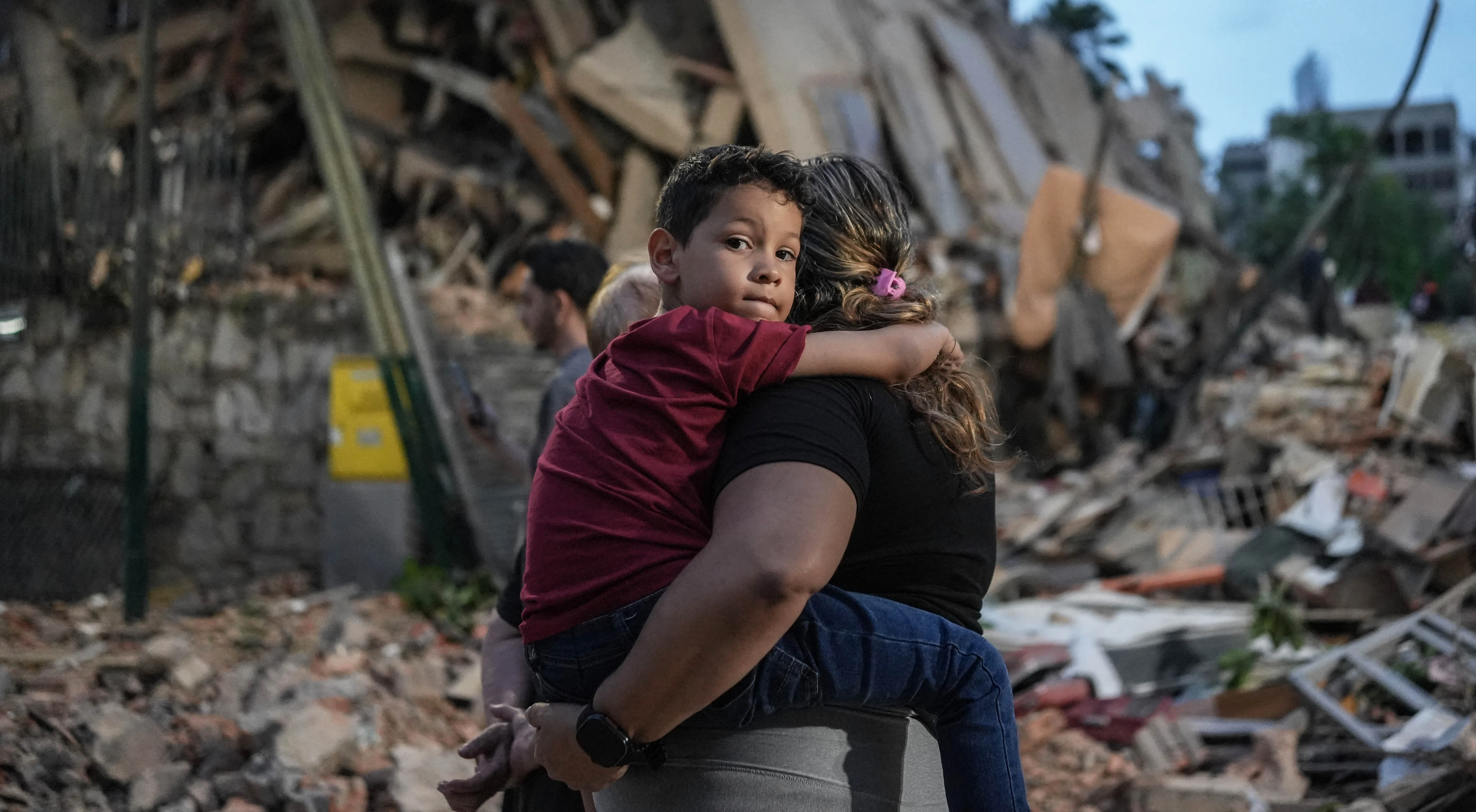 Mother holding child tightly in front of rubble caused by earthquake