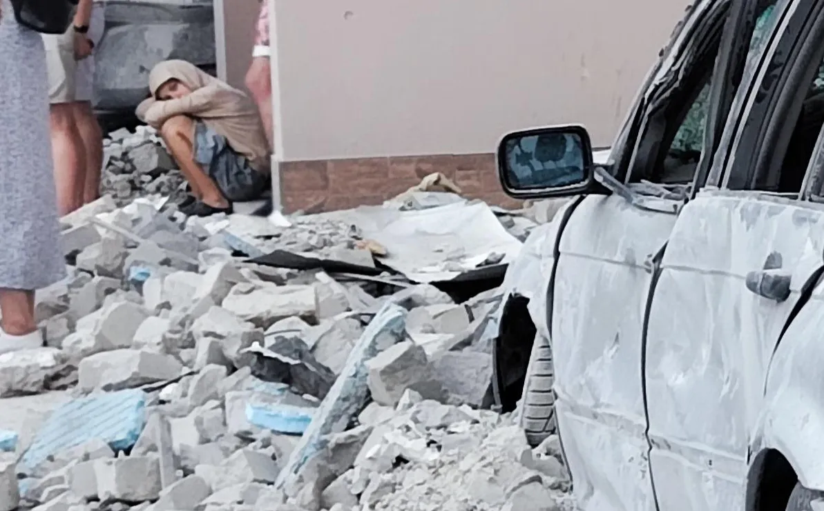Child sits quietly among the rubble outside a damaged building, head resting on folded arms, following the overnight attack in Kyiv.