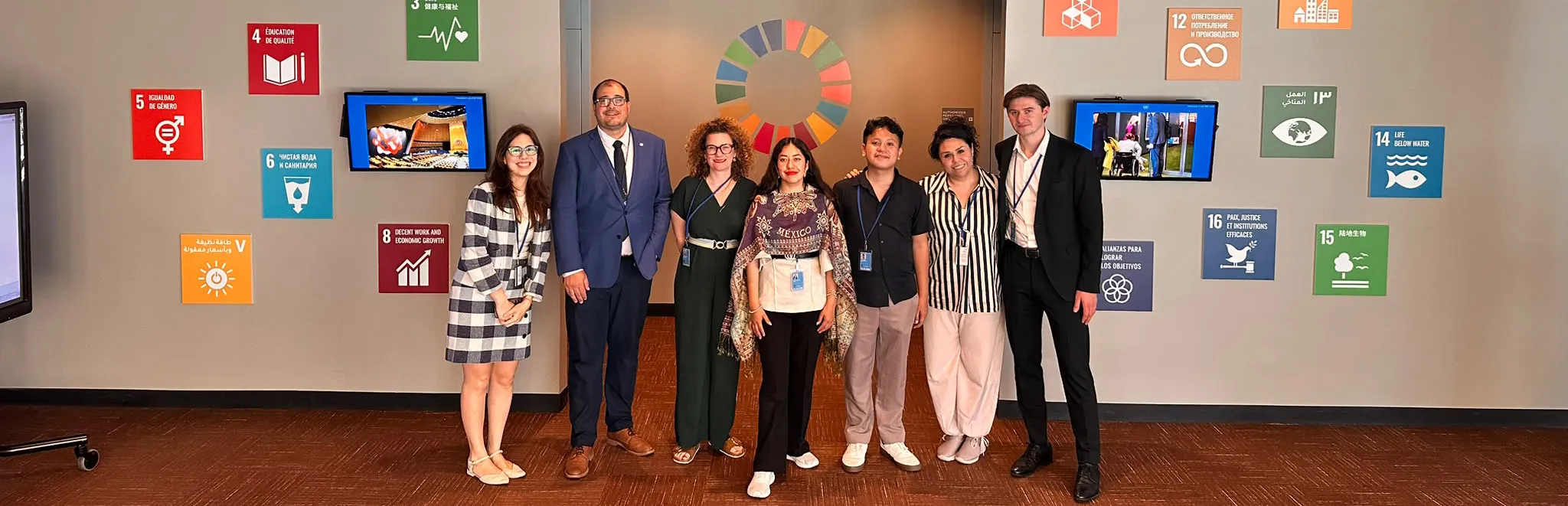 Seven delegates standing in front of a Sustainable Development Goals display at the United Nations in New York.