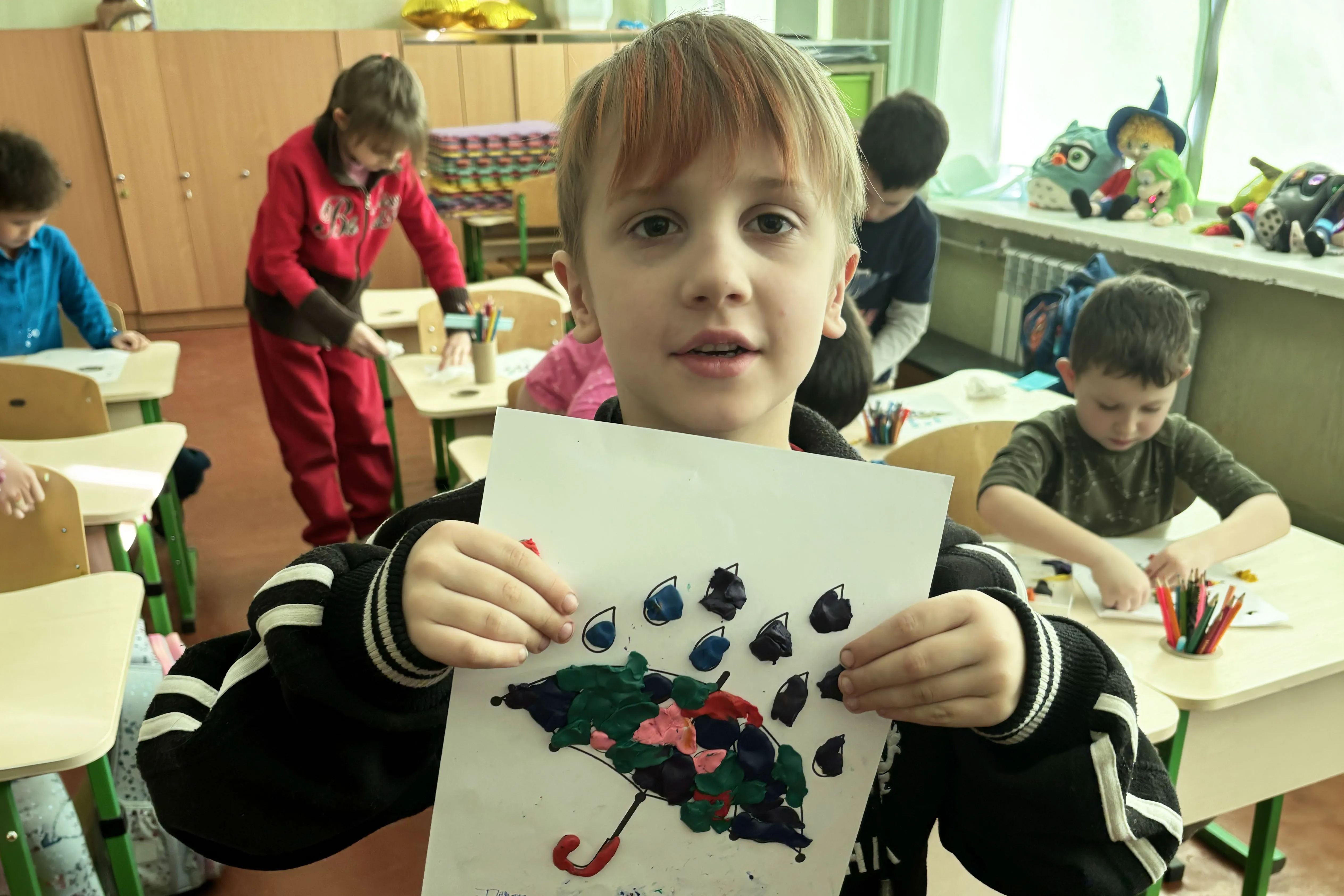 A young Ukrainian boy holding up a piece of art they have created.