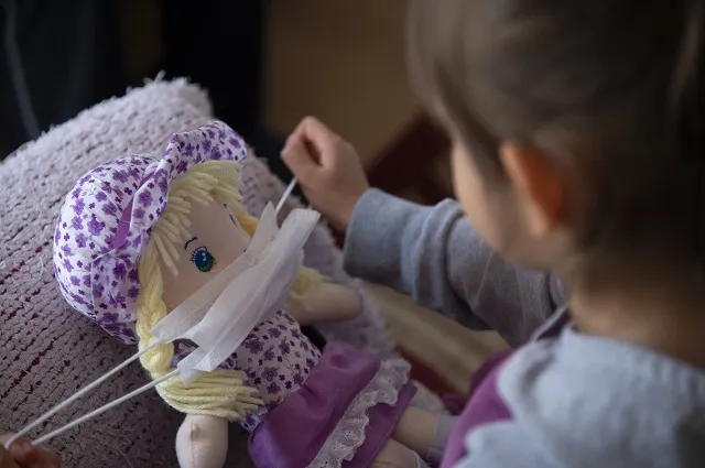 A child puts a protective mask on her toy.