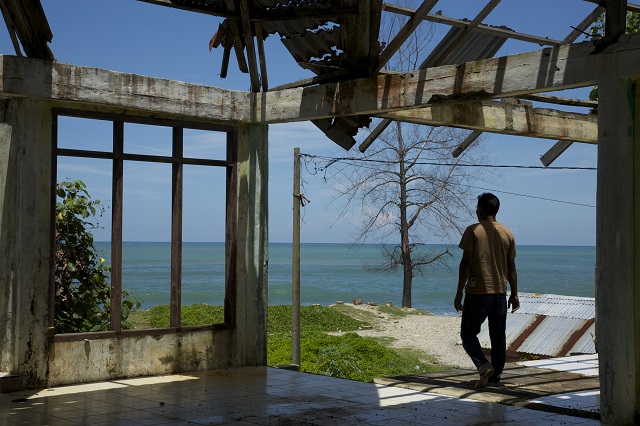 Un homme regarde depuis sa maison endommagée.